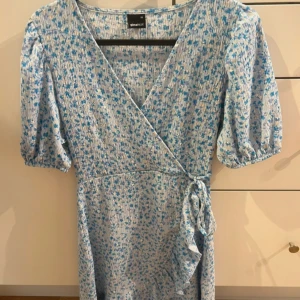 Blommig klänning från Gina Tricot - Supersöt klänning från Gina Tricot i ljusblått med små blå blommor. Klänningen har puffiga korta ärmar, v-ringning och knyt i midjan💗Använd fåtal gånger