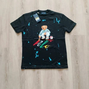 Svart Polo Ralph Lauren t-shirt med björn - Helt Ny! - Svart t-shirt från Polo Ralph Lauren med färgstarkt tryck av den ikoniska björnen som målar 'Polo' i rött, grönt, gult och vitt, storlek S | Skick: 10 / 10, aldrig använd! | Nypris: ~ 1400 (svår att få tag i!) | Vårt pris: 649 | Storlek: S | Tveka inte att höra av er med bud eller funderingar!
