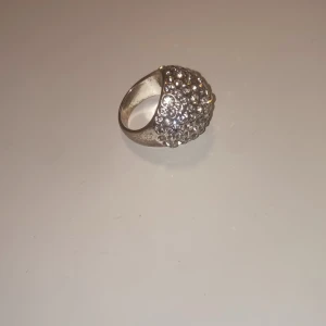Glittrig silverring med stenar - Säljer en chunky silverring som är täckt med massor av glittrande stenar. Ringen har en rundad, kupolformad design som verkligen sticker ut och fångar ljuset. Perfekt för dig som vill ha något extra bling på fingret och älskar statement-smycken.