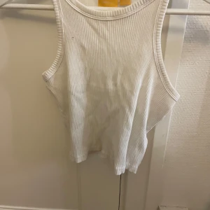 Vit ribbad linnetopp från Gina Tricot - Fräsch vit linnetopp från Gina Tricot i ribbad bomull. Modellen är ärmlös med rund hals och har en clean, croppad passform som är perfekt till jeans eller shorts. Enkel och stilren design som funkar till alla dina favoritoutfits.