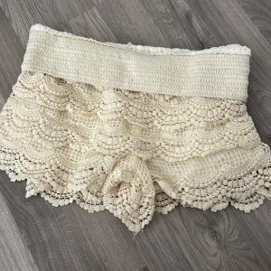 Beige virkade spets-shorts - Superfina beige shorts med bred resår i midjan och detaljerad virkad spets över hela plagget. De har en scallopad kant nedtill och ett romantiskt, boho-inspirerat utseende. Perfekta för varma dagar och festivalhäng. Materialet är mjukt och luftigt. Skulle säga att storleken är från xs-m 