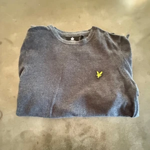 Mörkgrå stickad tröja från Lyle & Scott - Snygg mörkgrå stickad tröja från Lyle & Scott med klassisk gul fågel-logga på bröstet. Tröjan har rund hals, långa ärmar och ribbade muddar vid ärmslut och nederkant. Tröjan är ganska ny då det igentligen bara är att stryka den så är den som ny igen. Kontakta mig vid minsta bekymmer🙌
