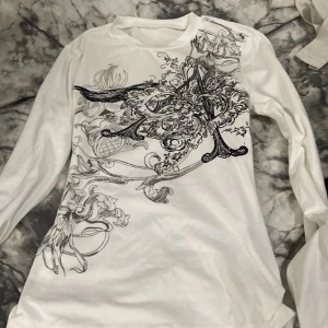 Vit långärmad tröja med print XS - Snygg vit långärmad tröja i storlek XS med ett stort, detaljerat svart print över framsidan. Tröjan är tillverkad i mjuk bomull med lite elastan för extra komfort. Passar dig som gillar coola grafiska mönster och vill ha en unik look. Från SHEIN