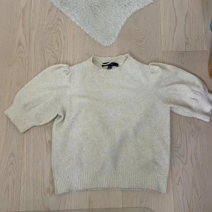 Beige stickad tröja med puffärm - Säljer en beige stickad tröja från Vero Moda med puffiga kortärmar och ribbade muddar. Tröjan har en rund halsringning och är gjord i mjukt material som känns skönt mot huden. Perfekt för dig som gillar enkel men trendig stil.