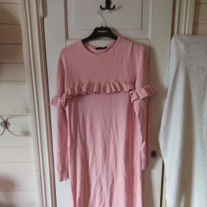 Ljusrosa långklänning med volang - En ljusrosa långklänning från Reflex med stickad struktur med en volang över bröstet och axlarna. Det är ett ganska tjockt material så man kan ha den i kallare väder.