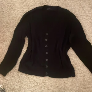 Mörkblå kofta från Brandy Melville - Blå, ribbad kofta från Brandy Melville med v-ringning och knappar hela vägen framtill.   Perfekt att slänga över en topp när det är lite kyligare ute.