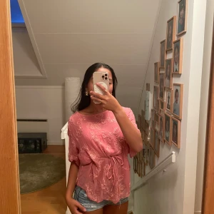 Rosa blommig blus med knytband - Säljer en söt rosa blus med blommigt mönster. Blusen har korta ärmar med lätt puff och ett knytband i midjan som ger en snygg siluett. Storlek är dock lite oklar typ S