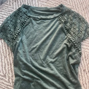 Grön blus med spetsdetaljer - Supersnygg grön blus med korta ärmar och spetsdetaljer över axlarna. Blusen är mjuk och skön, vet inte vart den är ifrån eftersom den har ärvts. 
