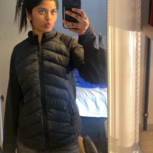 Svart pufferjacka med dragkedja - Svart pufferjacka med quiltad framsida och släta ärmar. Jackan har en hög krage och hel dragkedja framtill. Perfekt för kyliga dagar och har en modern, sportig look. Passformen är normal och jackan är lätt att matcha med olika outfits.