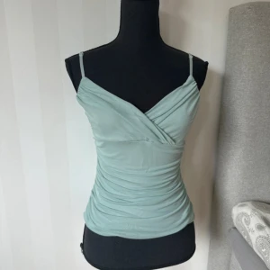 Turkos omlott linnetopp från Vila - Supersnygg turkos linnetopp från Vila med omlott-design framtill och smala justerbara axelband. Toppen har en tight passform och är gjord i mjuk polyester som sitter skönt mot kroppen. Perfekt att styla med jeans eller kjol för en fräsch look.