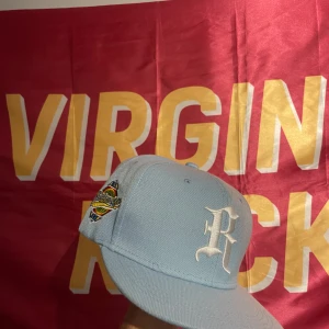 Ljusblå keps med broderad logga - Snygg ljusblå keps från Golden Age med vit broderad bokstav på fronten och färgglad broderad patch på sidan. Klassisk flat brim och strukturerad passform, perfekt för att lyfta din streetwear-look.