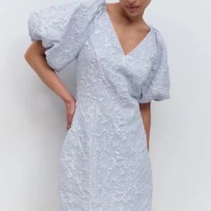 Ljusblå kortklänning med puffärm - Säljer en ljusblå kortklänning med v-ringning och stora puffärmar. Klänningen har ett vackert strukturerat blommigt mönster i tyget som ger en lyxig känsla. Passformen är normal och materialet känns som polyester. Prislapp kvar 