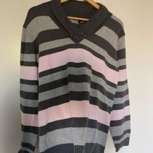 Randig stickad tröja från Isolde - Säljer en mysig stickad tröja från Isolde med breda ränder i grått, mörkgrått och ljusrosa. Tröjan har en bred ribbad krage med två knappar, långa ärmar och ribbade muddar. Perfekt för dig som gillar chill och snygg stil.Storlek enligt mig L-XL,märkt som XXL