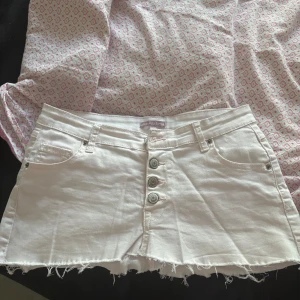 Vit jeanskjol från Sincerely Loved - Supersnygg ljusrosa  jeanskjol från Sincerely Loved i kort modell med fransad kant. Kjolen har fyra silverfärgade knappar framtill, klassiska fickor både fram och bak samt hällor för bälte. Perfekt för dig som gillar en chill och trendig stil.