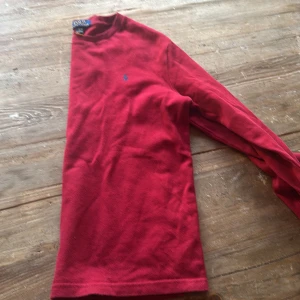 Röd långärmad tröja Polo Ralph Lauren - Säljer en röd långärmad tröja från Polo Ralph Lauren med klassisk blå broderad logga på bröstet. Tröjan är stickad i bomull och har en enkel, clean design med rund hals. Perfekt för dig som gillar stilrena märkesplagg. Säljer pga att den inte passar längre. Pris kan diskuteras 