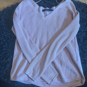 Ljusrosa stickad V-ringad tröja Vero Moda - Superfin ljusrosa stickad tröja från Vero Moda med V-ringning och långa ärmar. Tröjan har en ribbad struktur och är perfekt för lager-på-lager. Enkel att matcha med både jeans och kjol.