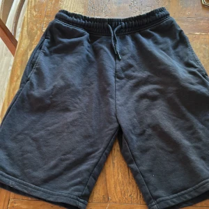 Svarta shorts från Next med snörning - Mysiga svarta shorts från Next med elastisk midja och snörning. Tillverkade i mjuk bomullsblandning med fickor på sidorna. Perfekta för chill dagar eller träning. Klassisk loose fit och enkel stil som funkar till det mesta.