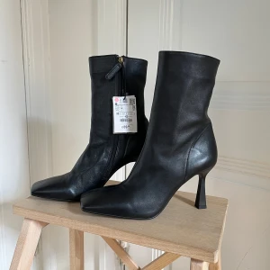 Svarta stövletter i läder Zara strl 39 - Snygga svarta stövletter från Zara i läder med markerad fyrkantig tå och hög smal klack. Dragkedja på insidan för enkel påtagning. Perfekt för dig som vill ha en stilren look.