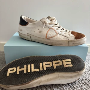 Philippe Model skor - Snygga vita sneakers från Philippe Model med bruna mockadetaljer på tån och svart hälparti. Skorna har snörning, klassisk låg profil och en cool logga på sidan. 