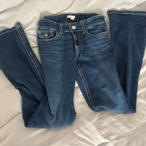 Blå bootcut jeans med kontrastsömmar - Snygga blå jeans med bootcut passform och markerade vita kontrastsömmar. Klassiska femficksdetaljer och ficklock med knapp bak. Jeansen har en normal midja och är tillverkade i mjukt denimtyg som sitter skönt hela dagen.