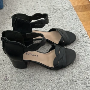 Svarta sandaler med klack från Via Spiga - Svarta sandaler från Via Spiga i skinn med flätad rem över tårna och öppen tå. Skorna har en stabil låg klack, dragkedja bak och en stilren design som passar perfekt till varma dagar. Snygga och bekväma med klassisk look. Typ aldrig använda, står 34,5 men skulle säga att de är lite större❤️