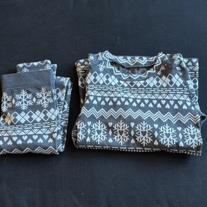 Grå tröja med snöflingor och hjärtan - Mysig grå tröja med vitt vintermönster av snöflingor, hjärtan och geometriska former. Perfekt för kalla dagar och julmys. Tröjan har rund hals och är långärmad, i mjukt bomullsmaterial som känns skönt mot huden.