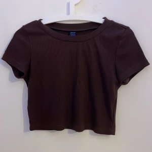 Brun croppad topp från SHEIN - En mörk brun croppad topp från SHEIN med korta ärmar och rund hals. Toppen är ribbad och har en enkel och funkar bra som ett basplagg. Materialet är mjukt och stretchigt för en bekväm passform.