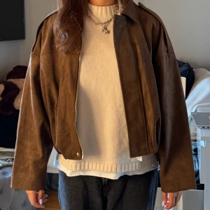 Brun mocka bomberjacka - Snygg brun bomberjacka i mjuk mocka med oversized passform och långa ärmar. Jackan har krage och dragkedja framtill, perfekt för dig som gillar en chill och trendig stil. Passar till både jeans och kjol för en cool look. Ny med prislapp!!
