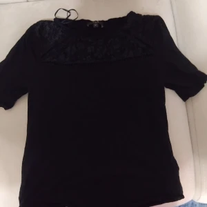 Svart spetsblus från 1.2.3 Paris - Supersnygg svart blus från 1.2.3 Paris med korta ärmar och vacker spets upptill. Blusen har en feminin och elegant look med genombrutna detaljer vid axlar och bröst. Perfekt för dig som gillar stilrena och trendiga plagg med det lilla extra.