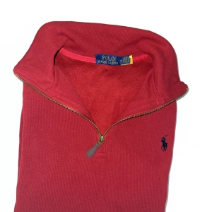 Röd tröja Polo Ralph Lauren - Snygg röd stickad tröja från Polo Ralph Lauren med half zip och klassisk broderad logga på bröstet. Tröjan har hög krage och är tillverkad i mjuk bomull, perfekt för lager-på-lager. Passar dig som gillar stilren och tidlös design.