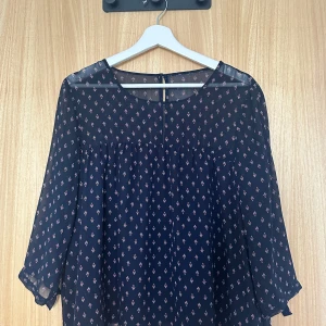 Mörkblå blommig blus med knytärm - Supersöt mörkblå blus i transparent polyester med små blommiga mönster i vitt och rött. Blusen har trekvartsärmar med knyt vid ärmslut och en knapp i nacken. En riktig Scandinavian style topp 🌸