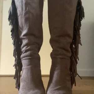 klackskor med fransar - Snygga höga stövlar i brun mocka med fransar längs utsidan. De har en rejäl blockklack och rund tå, vilket ger en cool och trendig look. Perfekta för dig som vill sticka ut med detaljer och älskar stockholmsstil/booho vibbar.