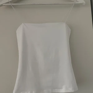 Vit enkel linnetopp med smala band - Säljer en stilren vit linnetopp med tunna axelband och rak skärning. Perfekt för varma dagar eller att styla lager på lager. Tidlös och clean look som passar till det mesta. Är i storlek xss men passar xs-s pga jätte elastisk 
