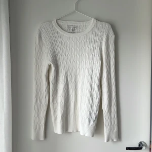 Vit kabelstickad tröja Gianni Feraud - Vit kabelstickad tröja från Gianni Feraud med rund halsringning och långa ärmar. Tröjan har klassiskt mönster och är gjord i mjuk bomull, perfekt för lager-på-lager under kyliga dagar. Enkel och stilren design som funkar till allt.