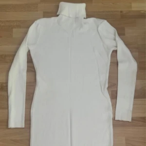 Vit ribbad långärmad poloklänning - Som ny. Säljer en vit långärmad klänning med polokrage och ribbad struktur. Klänningen är figurnära och har en enkel, stilren design som passar dig som gillar minimalistiskt mode. Materialet är mjukt och stretchigt, perfekt för att hålla dig bekväm och snygg. Använd en gång. Storlek lappar saknas, men den är L/XL, längd 115cm. 