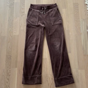 Bruna Juicy Couture byxor XXS - Säljer ett par bruna byxor från Juicy Couture i storlek XXS. Byxorna har bred resår i midjan med snörning, stora fickor fram och bak med knappdetaljer. Modellen är rak och loose med mjuk känsla, bra och mjuka mys byxor. De är uppsydda en bit, så lite kortare en vanligt. Men det är såklart på insidan så syns inte när du har på dem. Säljer för att jag har ett par svarta som används mer. Kan diskutera priset. 