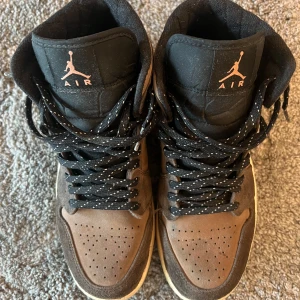 Nike Air Jordan 1 High Brun/Svart - Säljer ett par Nike Air Jordan 1 High i brunt och svart mocka med svarta detaljer och vit sula. Perfekta för dig som gillar streetwear. Skick: 8/10. Låda ingår. 
