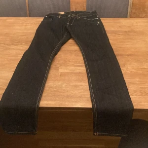 Mörkblå jeans från Dondup - Snygga mörkblå jeans från Dondup med klassisk femficksdesign och kontrastsömmar. Jeansen har raka ben och coola detaljer som metall-D och patch bak. Perfekta för dig som gillar stilrena och tidlösa jeans med premiumkänsla.