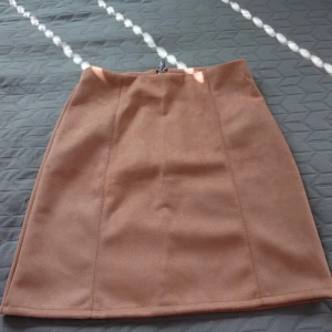 Beige mockakjol från Amisu - Snygg beige kortkjol från Amisu i mjuk mocka-look. Kjolen har en rak passform och en synlig dragkedja bak. Perfekt att matcha med boots eller en cool jacka. Enkel och stilren design som ger en chic vibe.