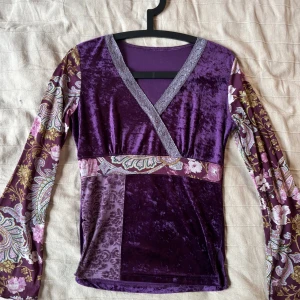 Lila omlottopp i sammet - Unik lila omlottopp i sammet med v-ringning och långa ärmar. På tredje bilden ser ni att den tyvärr har ett litet hål, därav så lågt pris! Men hålet märks knappt när man har på sig den och går absolut att bara sy igen om man vill det😉💓