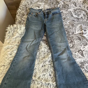 Blå bootcut jeans från 157, XXS - Snygga blå bootcut jeans från 157 i storlek XXS Short. Jeansen har låg midja och klassisk femficksdesign. Tillverkade i jeansmaterial med lätt slitning på låren för en cool look. Perfekta för dig som gillar retrovibbar och vill ha ett par riktigt schyssta bootcut.