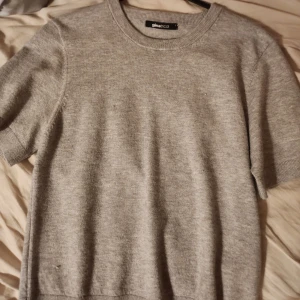 Grå stickad kortärmad tröja Gina Tricot - En enkel och stilren grå stickad tröja från Gina Tricot. Tröjan har korta ärmar, rund halsringning och är i mjukt material som känns skönt mot huden. Perfekt att matcha med jeans eller kjol för en clean look.