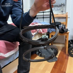 Mörkbrun nosgrimma med snokrem - Säljer ett stilrent mörkbrunt bälte i skinn med klassiskt spänne. Bältet har en slät yta och enkel design som passar till jeans eller kostymbyxor. Perfekt accessoar för att lyfta din outfit med en clean och tidlös look.