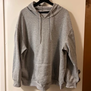 Grå hoodie med blå fjärilstryck - Grå oversized hoodie med stor blå och svart fjäril på ryggen och texten 'BUTTERFLY'. Hoodien har huva med snörning, magficka och långa ärmar. Perfekt för dig som gillar streetstyle och coola tryck.