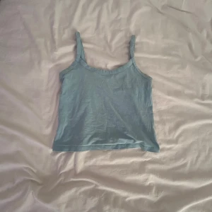 Ljusblå linnetopp från H&M Divided - En enkel och snygg ljusblå linnetopp från H&M Divided. Toppen är ärmlös med smala axelband och har en rak, croppad passform. Perfekt till sommaren och lätt att matcha med jeans eller kjol. Tillverkad i mjuk bomull för en skön känsla.