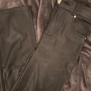 Svarta skinnbyxor från Bershka - Snygga svarta byxor i skinnimitation från Bershka. Klassisk femficksmodell med raka ben och silverfärgade detaljer. Perfekta för dig som vill ha en edgy look med stilren känsla. Materialet är mjukt och följsamt för extra komfort. 