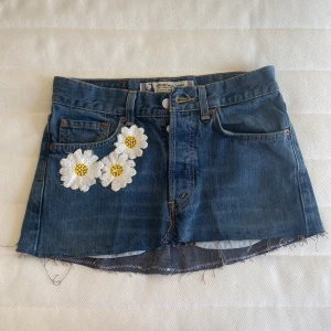Lågmidjad jeanskjol - Mörkblå jeanskjol från Crocker med rå kant och broderade vita och gula blommor framtill. Klassisk 5-ficksmodell med bälteshällor och dragkedja. Perfekt för dig som vill ha en cool och unik denimlook. Kontakta mig vid frågor💞😇står att storleken är w29, men den passar mig som bär xs/34.