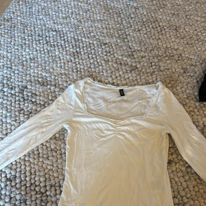 Vit ribbad långärmad topp H&M  - Supersöt vit långärmad topp från H&M Divided i ribbat material. Toppen har en snygg v-ringning med spetskant och rynkdetalj framtill. Passar till allt och är riktigt bekväm.