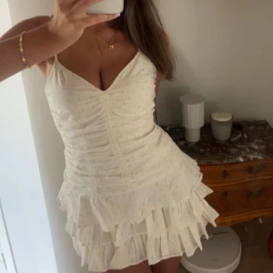 Vit kortklänning med volanger och guldprickar - Supersöt vit kortklänning med tunna axelband, v-ringning och volanger i flera lager. Klänningen har små guldprickar över hela tyget och rynkade detaljer framtill❣️