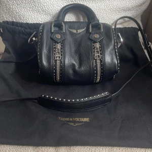  Zadig & Voltaire Sunny Nano Studs Bag ✨ - Säljer min fina Zadig & Voltaire-väska i svart läder med silverdetaljer. En ikonisk modell som passar lika bra till vardags som till fest.  🖤 Zadig & Voltaire, köpt i Paris september 2023 🖤 Svart läder med nitar och dragkedjedetaljer 🖤 Avtagbar och justerbar axelrem för crossbody/axel 🖤 Kommer med original dustbag 🖤 I mycket fint skick – knappt använd  Nypris ca. 3800kr Mitt pris:  2600kr